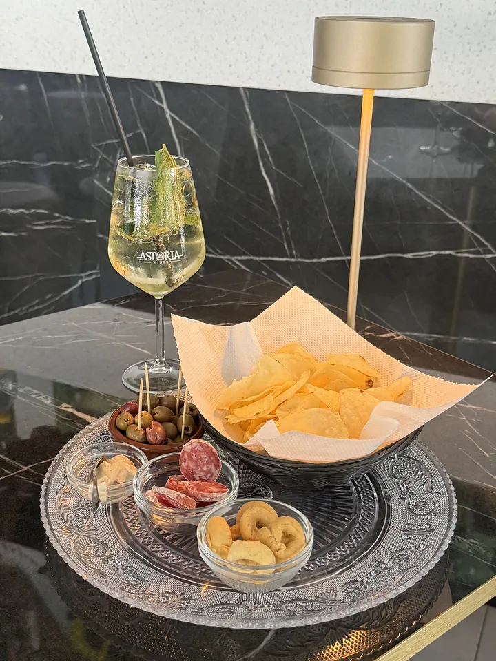 Calice di bollicine con menta e ghiaccio accanto a un tagliere con patatine, olive, salame e taralli