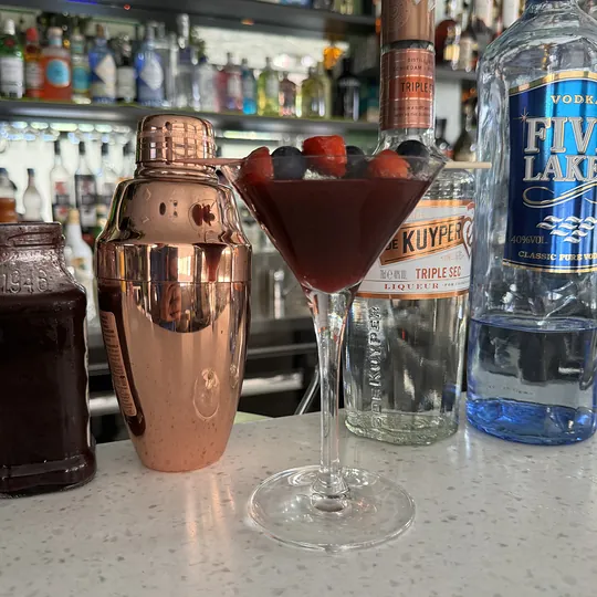 Cocktail ai frutti di bosco sul bancone, accanto allo shaker e alle bottiglie