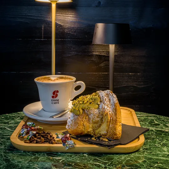 Cornetto al pistacchio tagliato a metà accanto al cappuccino
